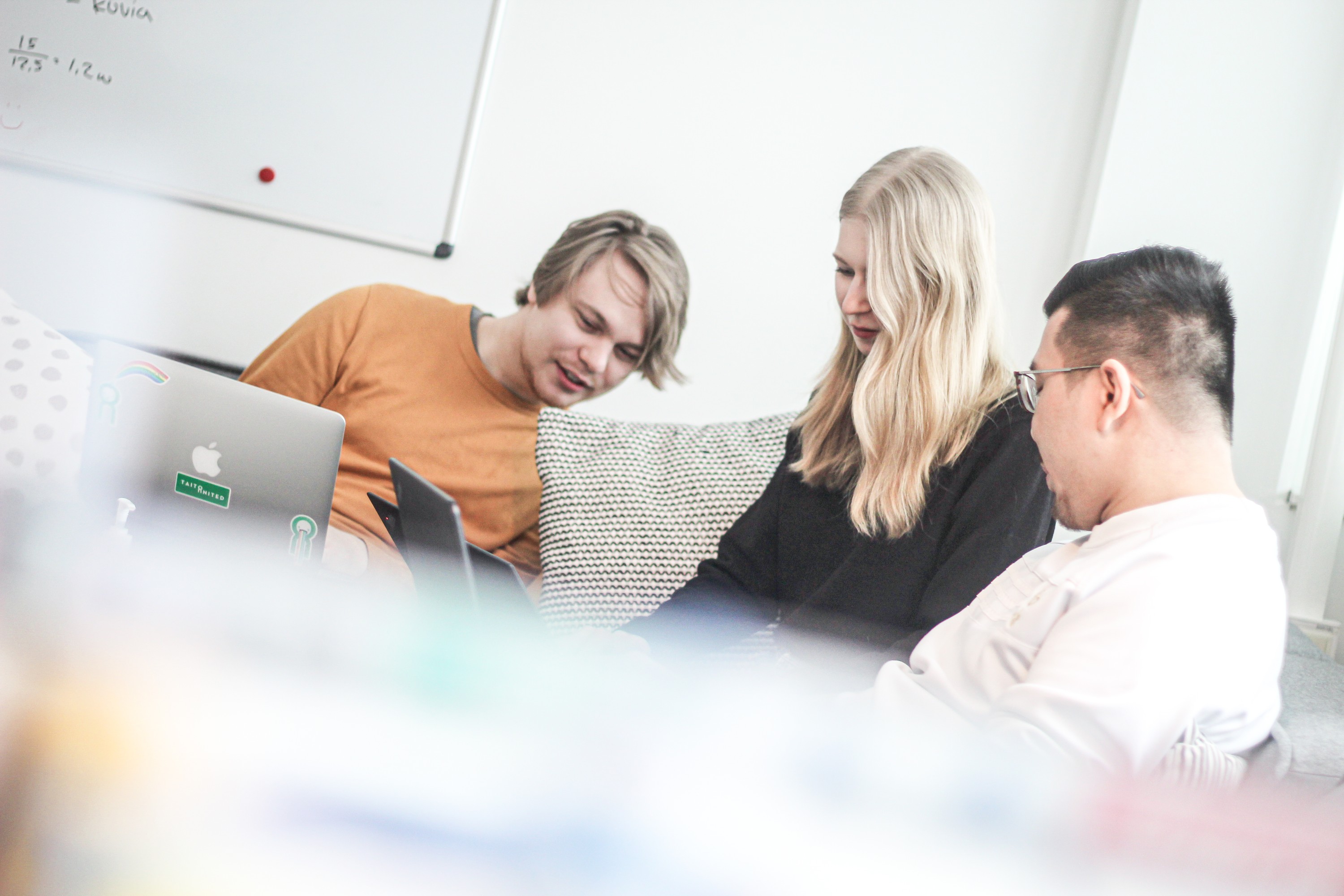 Two men and a woman looking at a laptop on the couch